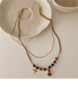 Detail of double-layer gold necklace with brown beads, star and oval pendants