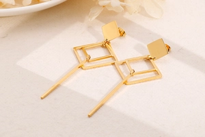 Detailed view of geometric hollow rhombus earrings in gold on stone surface
