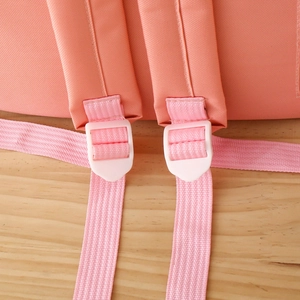 Detail of adjustable padded shoulder straps on an orange-pink canvas backpack for students