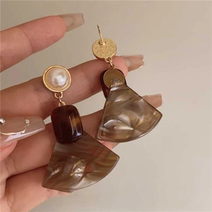 Detail of asymmetric resin earrings with tortoiseshell texture and pearl accents