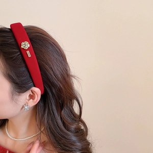 Détail d'un serre-tête en velours rouge avec rose dorée et accessoires métalliques latéraux