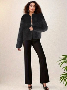 Full view of woman in black faux fur short jacket and wide-leg pants against neutral wall