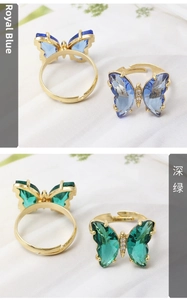 Close-up of butterfly rings with blue and green crystals on adjustable gold bands