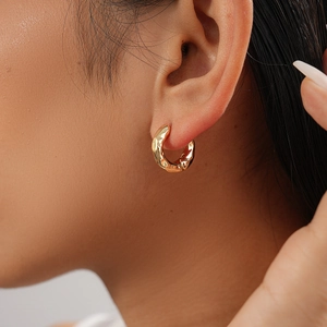Close-up of golden round earrings with irregular molten texture on woman ear