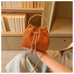 Close-up of sparkling orange rhinestone bucket bag with golden metal handle and tassels