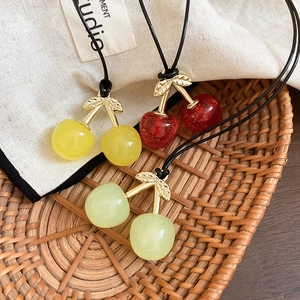 Detail view of colorful cherry pendants on black wax cords with leaf metal accents