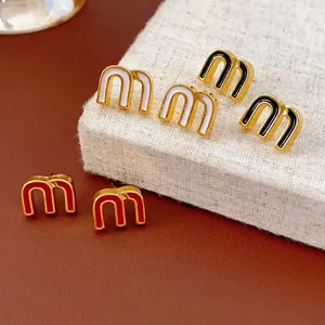 Letter m stud earrings in black, white, and red enamel with elegant gold-tone edges