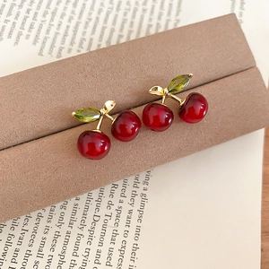 Close-up of cherry stud earrings with red resin beads and green zircon leaves