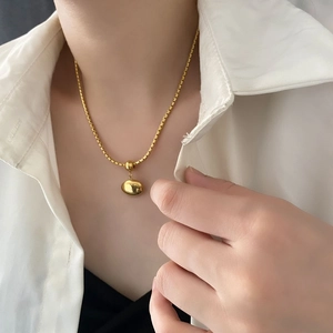 Gold pebble pendant necklace on a model wearing a white shirt in a minimalist style
