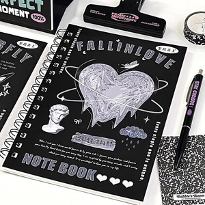 Detailed close-up of A5 black spiral notebook with holographic heart on a white desk