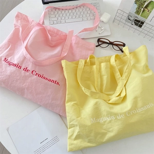 Flat lay of pink and yellow canvas tote bags with French print and laptop on white desk