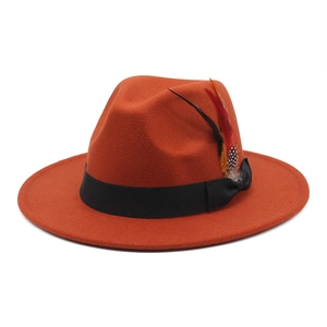 Detail of orange wool felt fedora featuring a black ribbon and decorative feather accessory