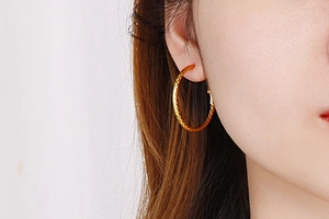 Detail shot of oversized gold hoop earrings with faceted texture worn by a model