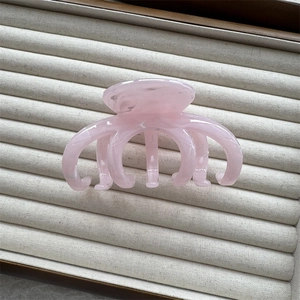 Close-up of pink translucent resin claw clip with cloud texture on grey display box