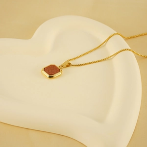 Gros plan du collier en acier titane doré avec pendentif en grès brun sur plateau