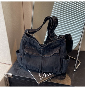 Detail of vintage black denim tote bag with large utility pockets on a dark wood surface