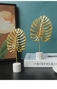 Detail showing golden monstera leaf metal ornaments with white marble bases for home decor