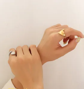 Detail showing asymmetric fluid-wave gold and silver rings on a hand in a minimalist style