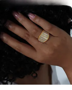 Detailed view of a wide gold-plated ring with white mother-of-pearl shell inlay on a hand