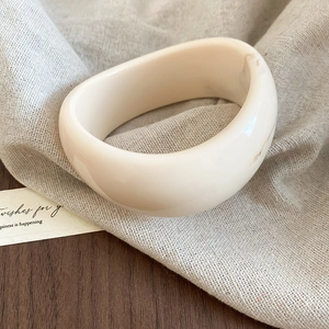 Macro shot of wide irregular cream acrylic resin cuff bracelet on linen fabric