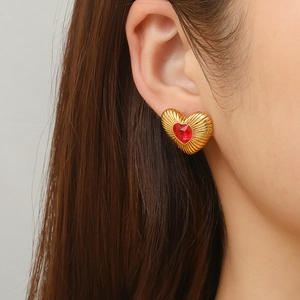 Elegant gold heart earrings with red crystal stone and radiant texture on model