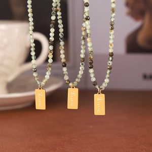 Peridot green beaded necklace with gold engraved Love pendant on a cozy background