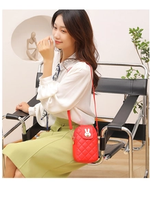 Detail of red quilted phone crossbody bag featuring a golden bunny-shaped metal clasp