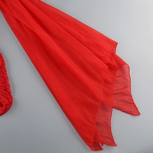 Vue détaillée du tissu mousseline rouge avec bords ondulés superposés et drapé fluide