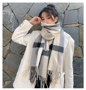 Detail of gray and beige plaid cashmere-like scarf with long fringe on white coat