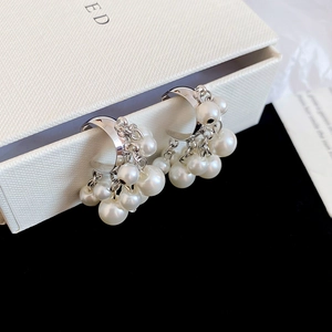 Detail of silver C-shaped beaded tassel earrings with white pearls on a white jewelry box
