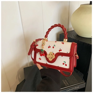 Detail of white cherry print handbag with red leather trim and golden flower clasp