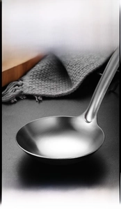 Macro detail of the deep stainless steel soup ladle with brushed metal finish and sturdy handle