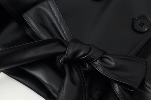 Makro-Detail einer schwarzen Lederjacke mit Gürtelknoten und passendem Knopf-Detail