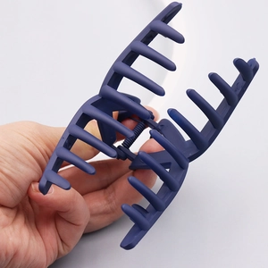 Matte deep blue large hair claw clip in hand for styling, minimalist aesthetic