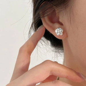 Detail of elegant silver rose flower stud earring worn on ear with polished finish