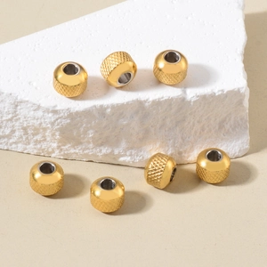 Macro shot of seven golden diamond-textured stainless steel spacer beads on a stone base