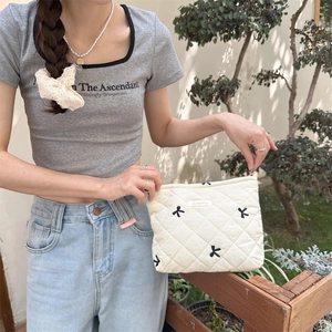 Detailed view of quilted makeup bag with bow embroidery held by a model in sunlight