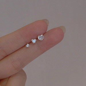 Three sizes of heart-shaped gold stud earrings shown on fingers for scale comparison