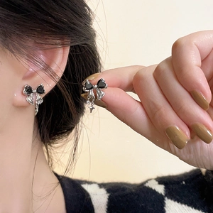 Close-up of silver bow earrings with black heart stones and tassels worn by a model
