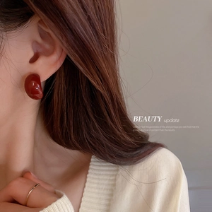 Deep red geometric heart earrings with smooth glossy finish worn by a model in beige knitwear