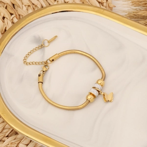 Détail du bracelet chaîne serpent dorée avec papillon et strass sur marbre chic