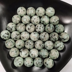 Close-up of polished green aventurine crystal spheres in a black curved decorative bowl