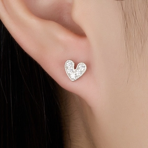 Détail macro d'une boucle d'oreille cœur en argent 925 avec des pierres de zircone claires
