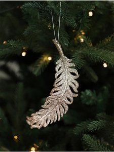 Champagne gold feather Christmas ornament with glitter finish hanging on a festive tree