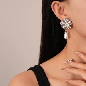 Detail of flower earrings with crystals and pearl pendants worn by a female model