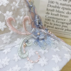 Close-up of intricate floral embroidery and pearl accents on white lace mesh fabric