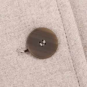 Dettaglio macro del tessuto intrecciato beige e bottone opaco marrone scuro sul cappotto