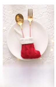Close-up of red knit Christmas stocking cutlery holder with golden fork and spoon on plate