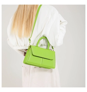 Green leather tote bag with top handle worn on shoulder by model in white jacket