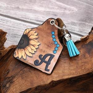 Western style leather sunflower initial A keychain with blue tassel on wood surface